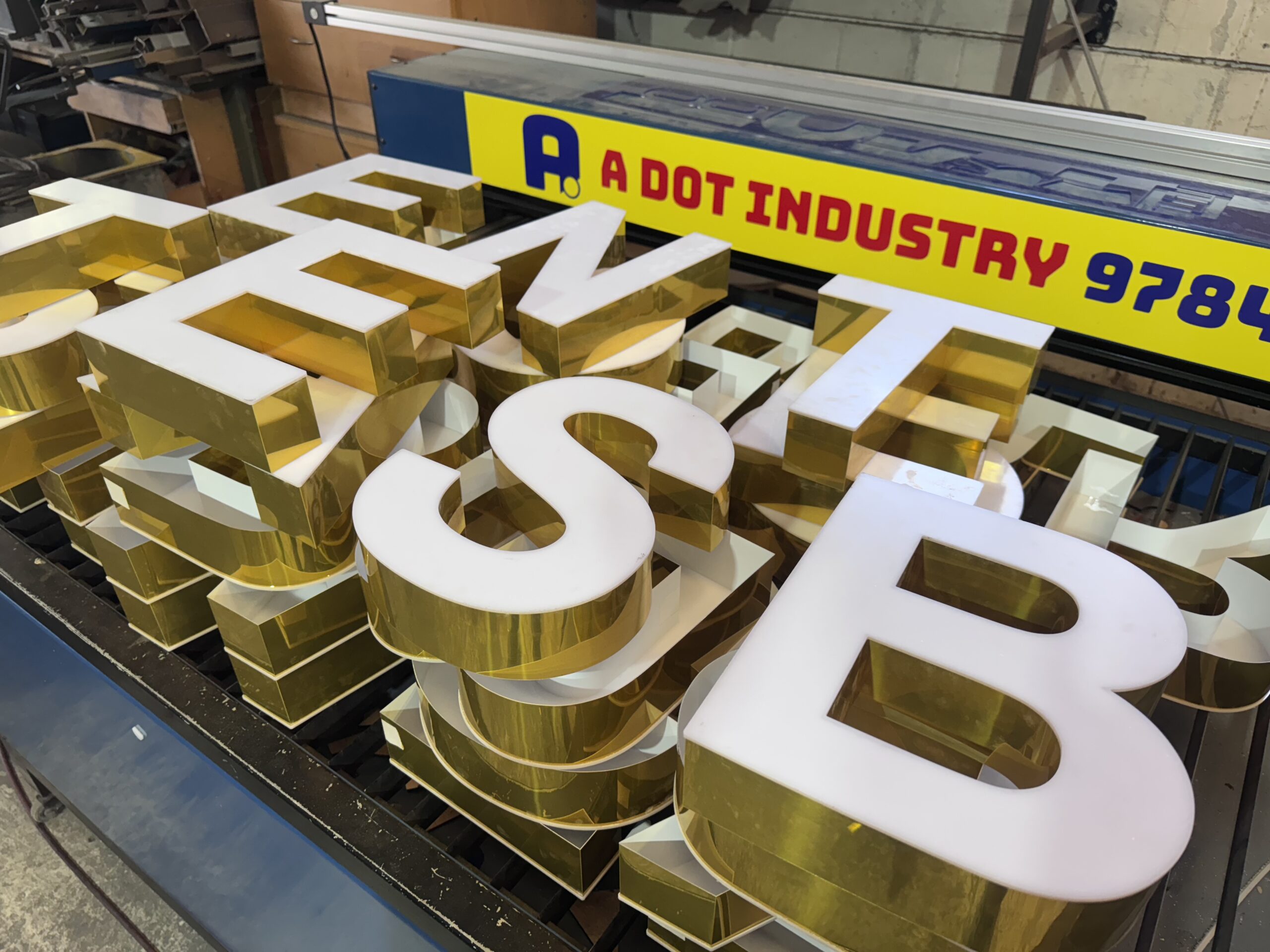 Stack of gold-colored 3D letters for signage on a worktable.