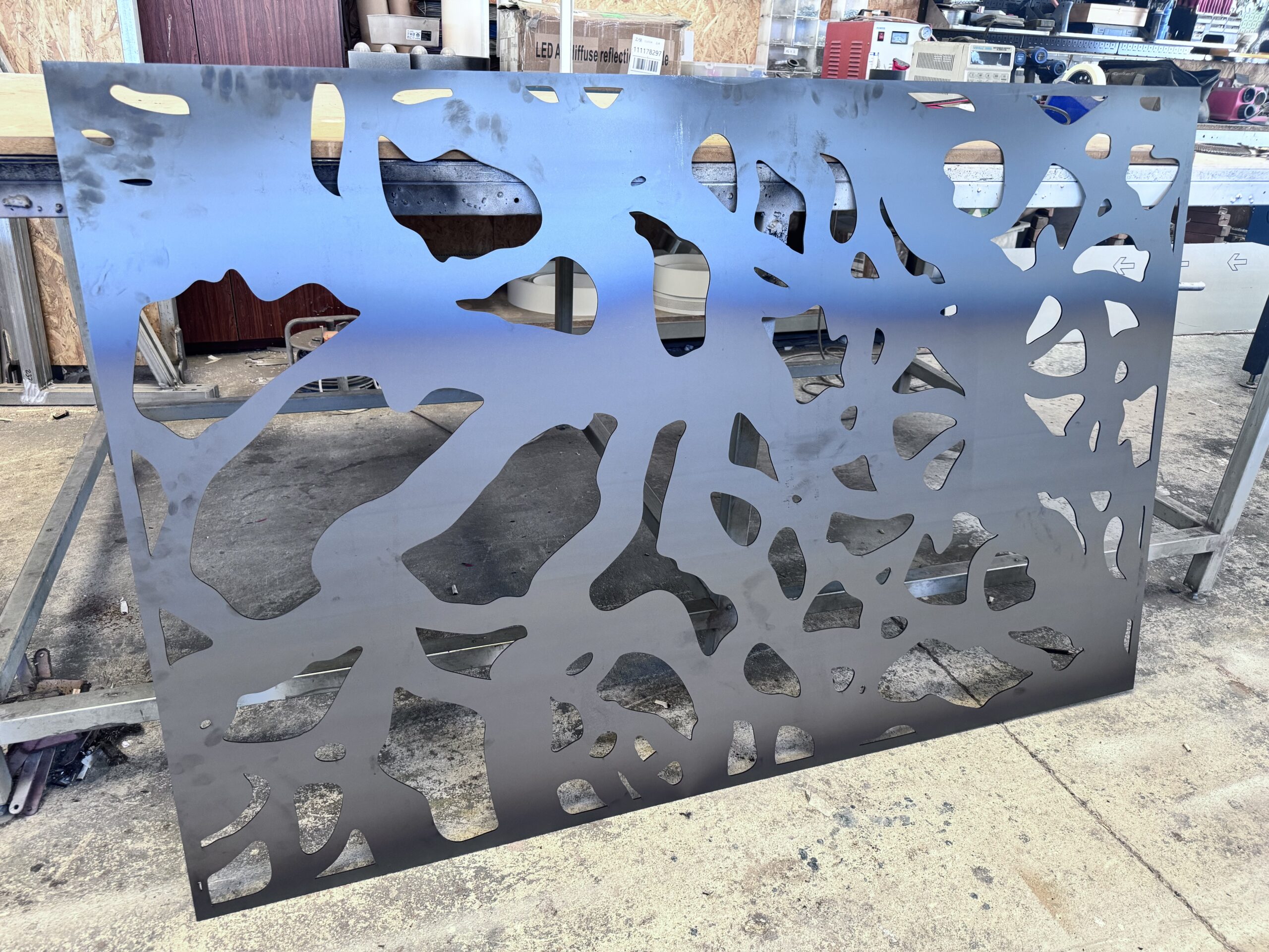 Laser cut steel panel with abstract design on workshop floor.