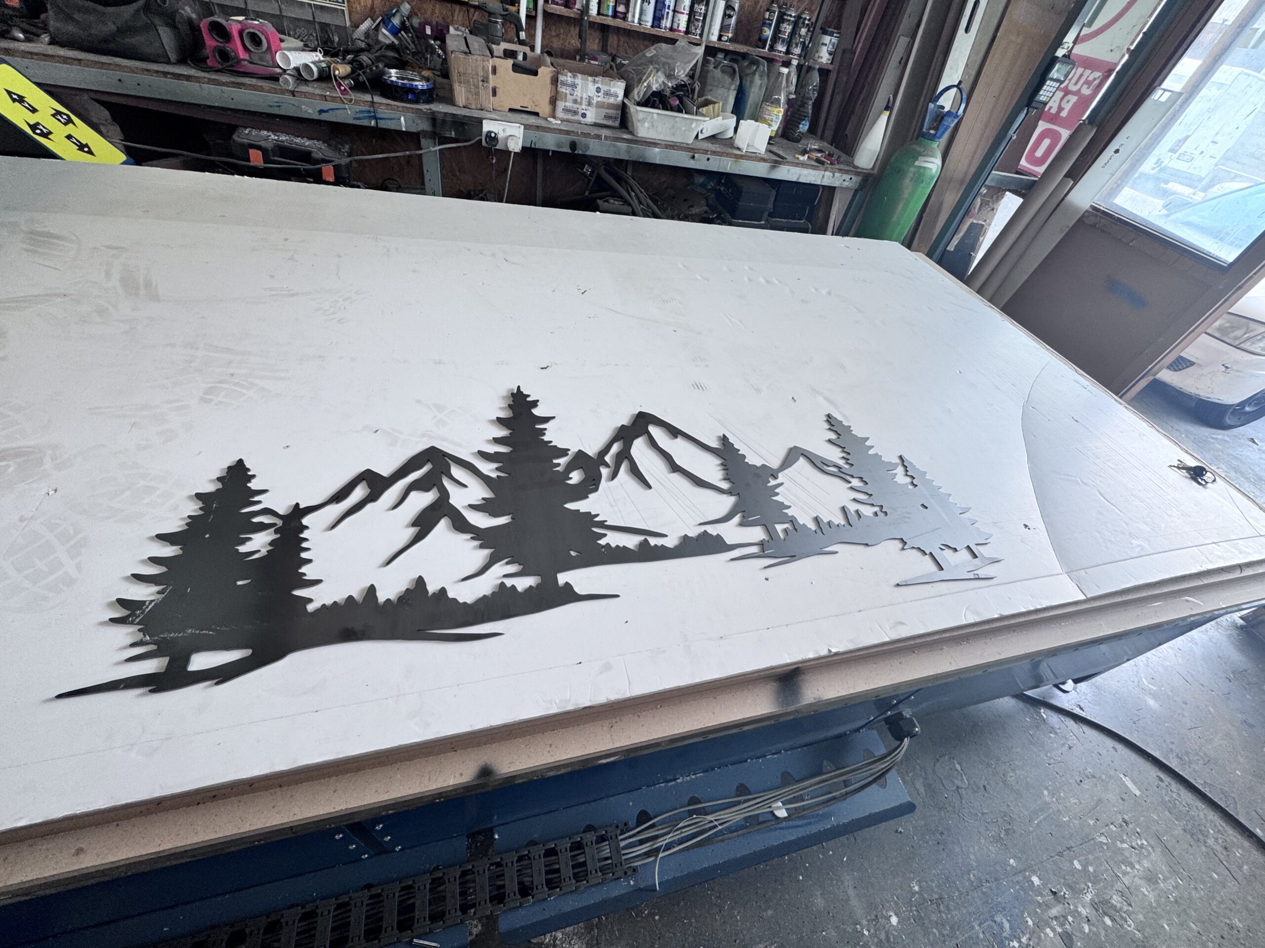 Metal art piece depicting mountains and trees on a workshop table.